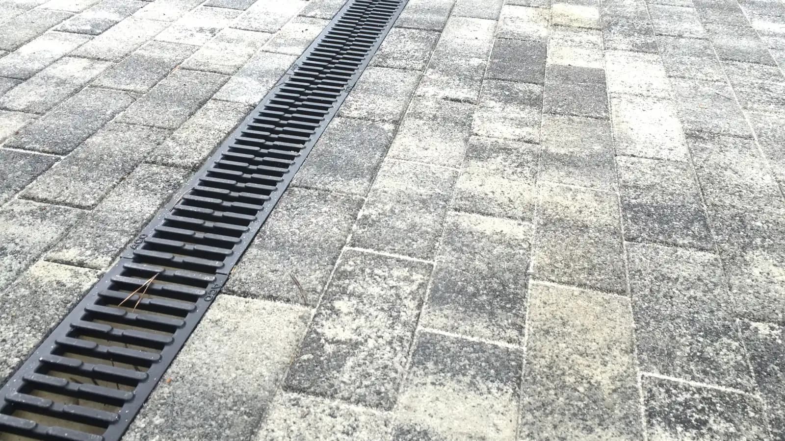 Серая тротуарная плитка крупным планом с чёрной водоотводной решёткой посередине