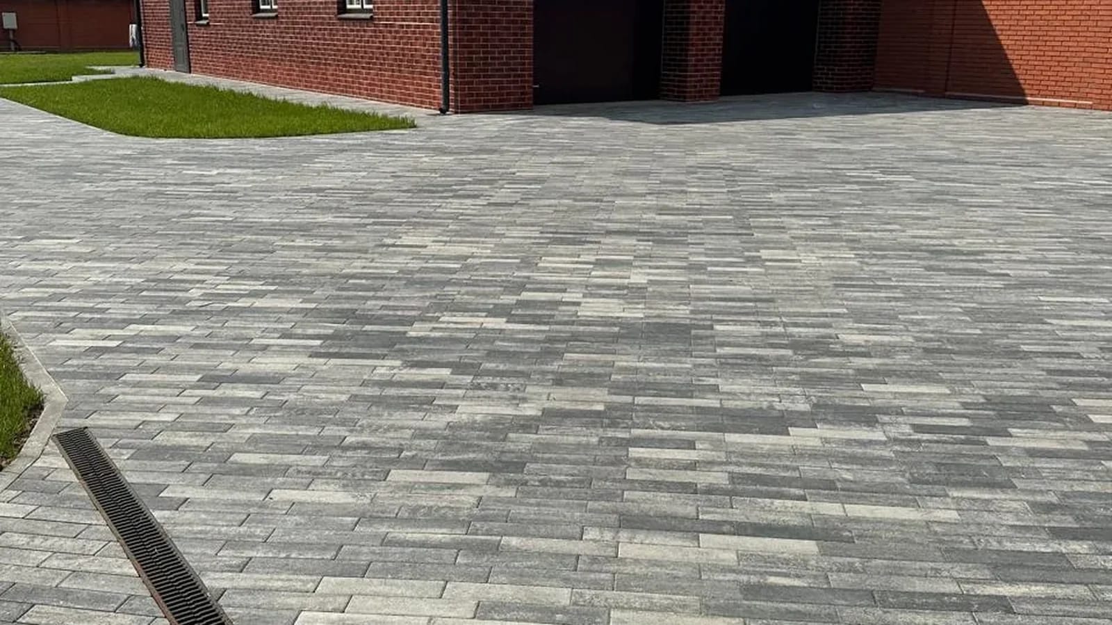 Широкая площадка из серой брусчатки-кирпичика перед краснокирпичным домом с гаражом, в мощение врезан водоотводный лоток